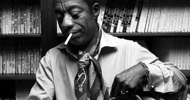 a black man with a cigarette in his mouth, sitting and looking down.
