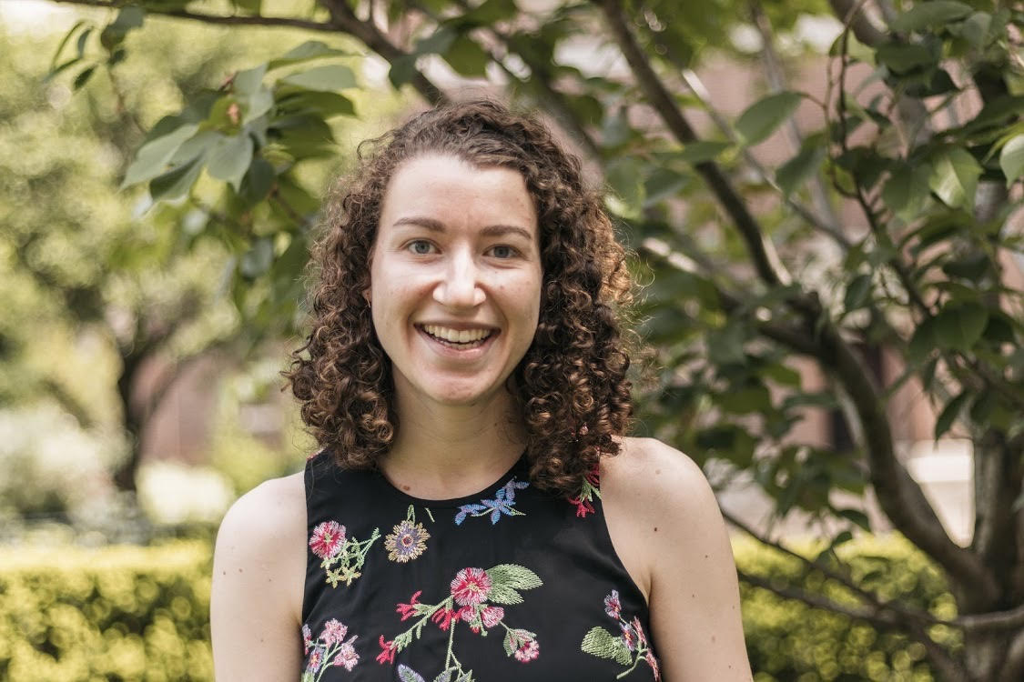 Jodi pictuted outside in front of a blooming tree wearing a floral dress