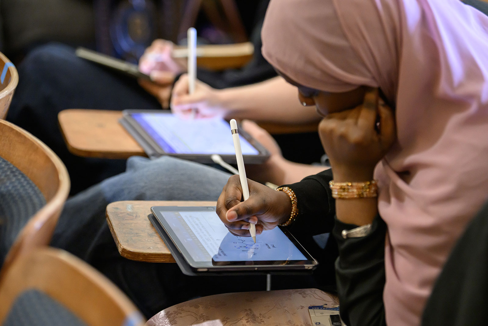 Student at desk writing on tablet