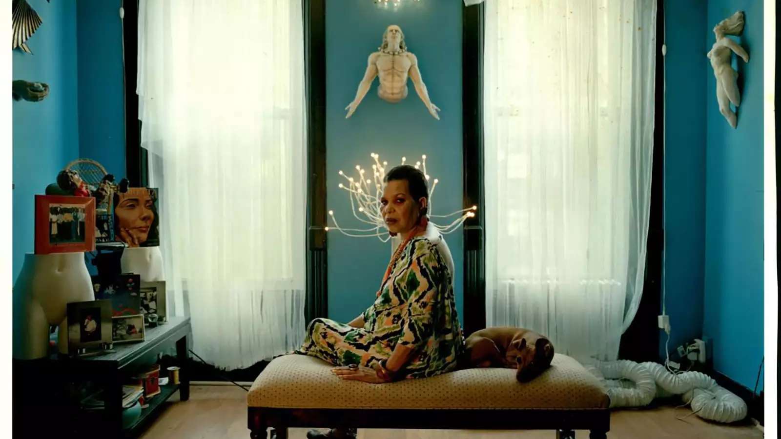 Ntozake Shange sitting on a bench in a beautiful room, looking over her shoulder at the viewer